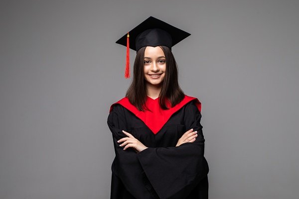 Studio portrait of funny excited joyful student girl with graduation certificate. Happy academy, college or university graduate standing against gray background, holding diploma and smiling at camera